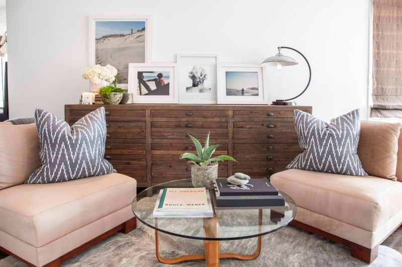 Beach house living room with organic design elements, rustic wood chest of drawers, uniform white frames.