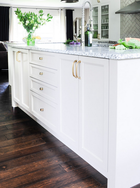 Kitchen by 2e designs with brass hardware, white island, and dark wood floors. 