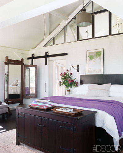 Meg Ryan's master bedroom with exposed beams, hanging sconce, sliding barn door, and vintage trunk 