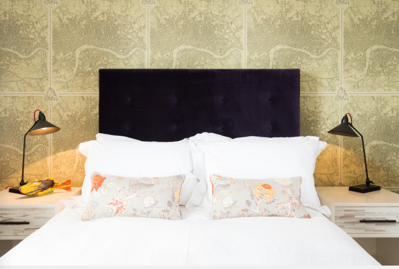 Gorgeous bedroom with map wallpaper, velvet headboard, and white linens. 