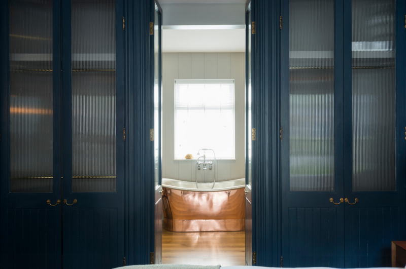 Total class and a bit of drama: custom navy wardrobes and a copper bathtub. 