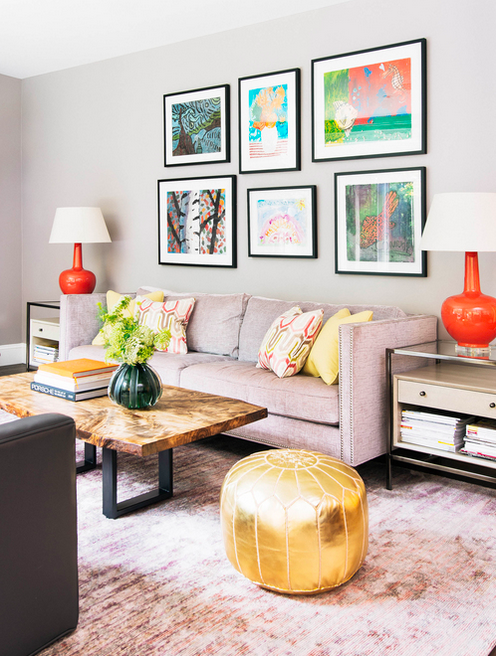 Framed art, bright colored lamps, dusty rose sofa, rustic wood coffee table, and gold pouf. 