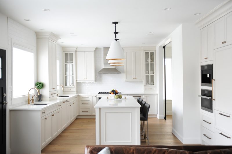 Beautiful white kitchen with large island, bar stools, and brass fixtures. 