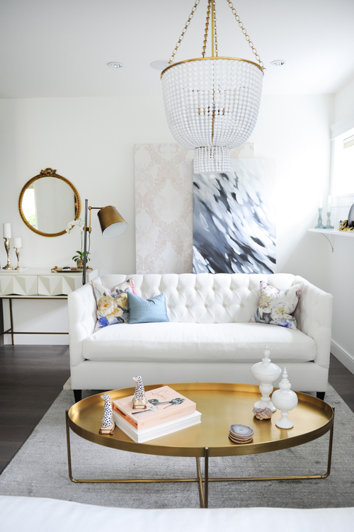This living space is small but stylish comfortable thanks to its white tufted sofa, gold, oval coffee table, and layered artwork.